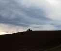 Shadow of tractor on dark horizon of field with grey sky above