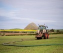 Tractor in a field spreading slurry with fields in the background and hills on the horizon.